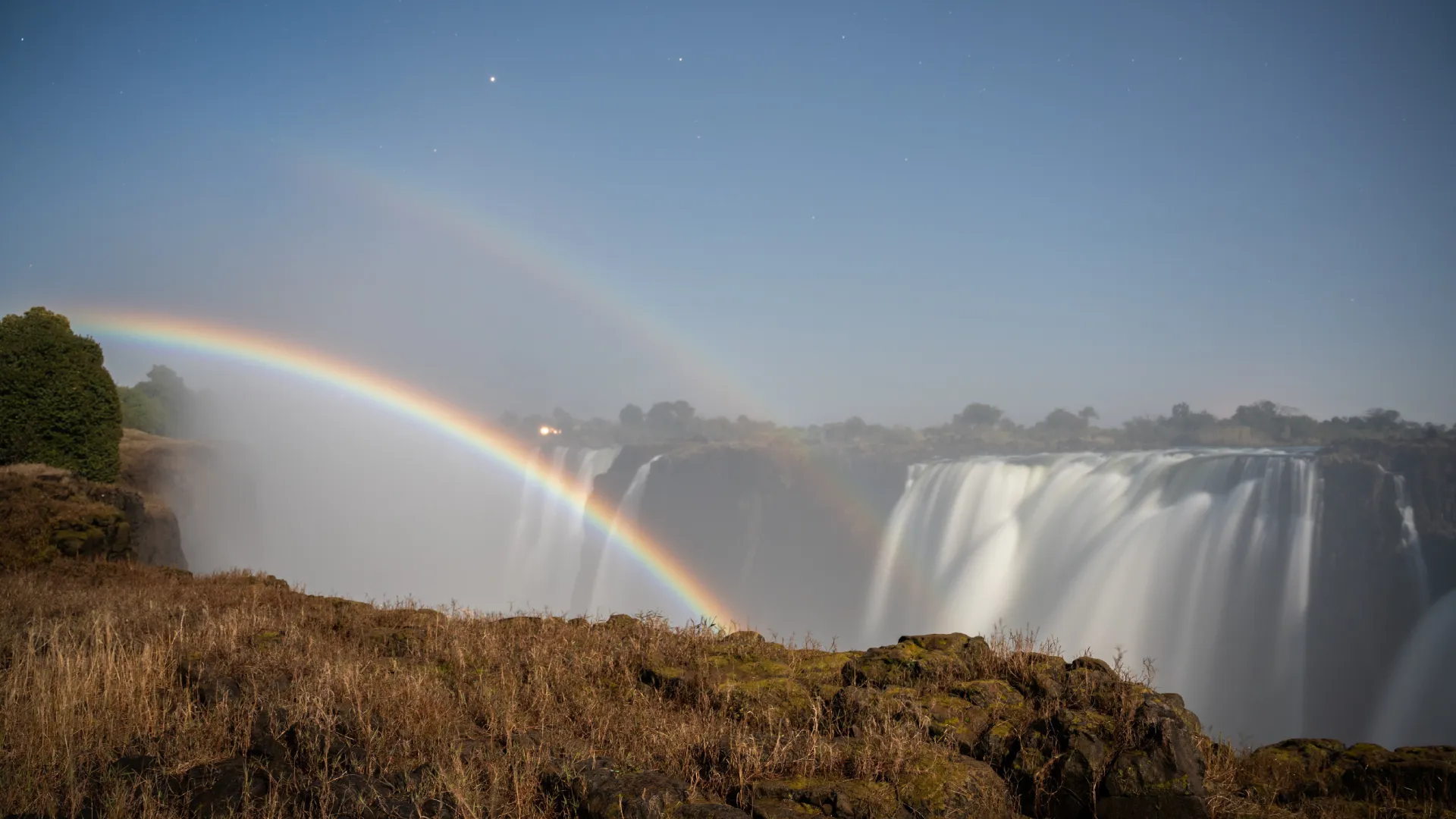 Lunar rainbow (moonbow) arching over Victoria Falls at night during a full moon