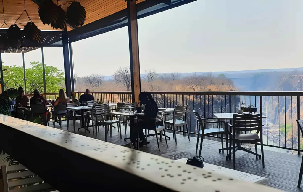 Close-up of the Braille railing at The Lookout Café with fingertips tracing the embossed text and the gorge softly out of focus behind