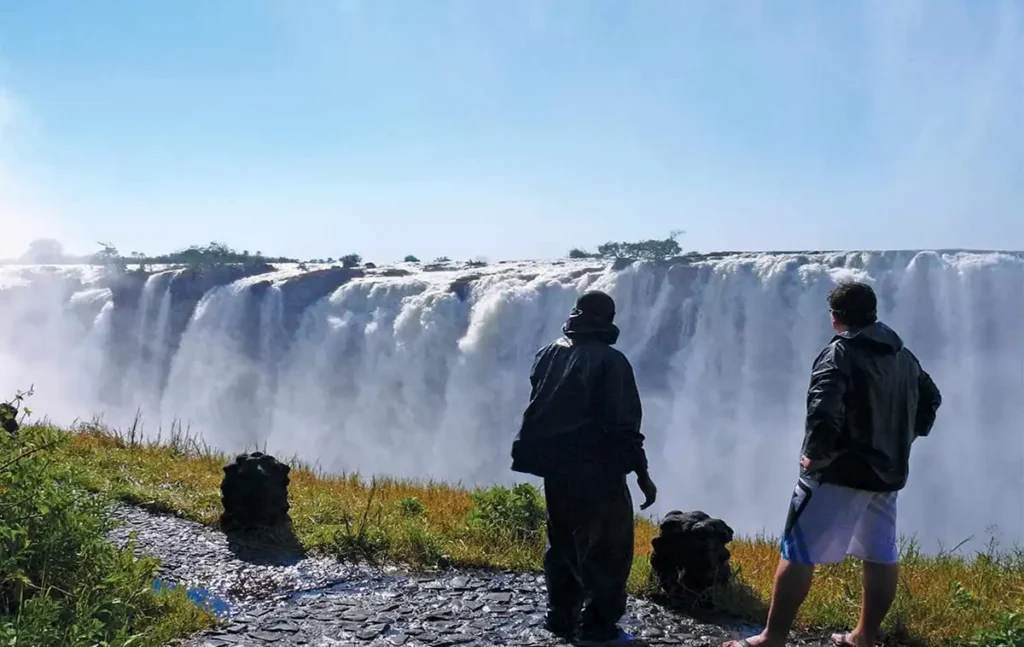 Wild Horizons guests in raincoats at a Victoria Falls viewpoint with mist and a rainbow in the spray