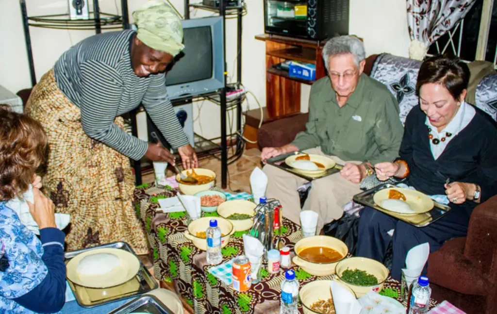 Guests sharing a meal of sadza and stew with a host family in a rural Zimbabwean kitchen