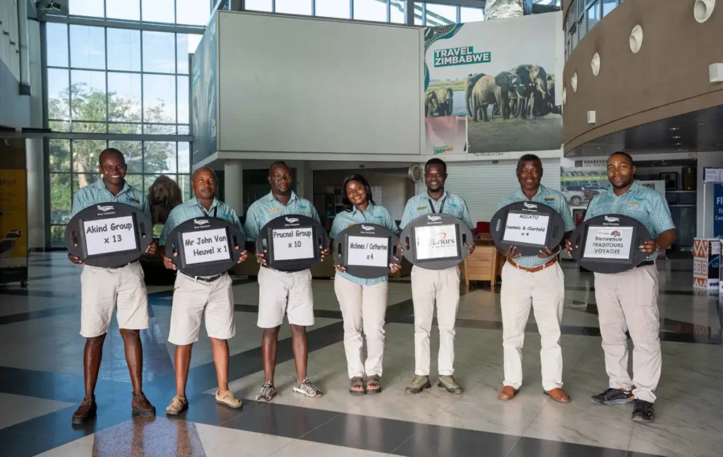 A Wild Horizons driver in a light blue branded shirt holding a welcome board in the Victoria Falls Airport arrivals hall