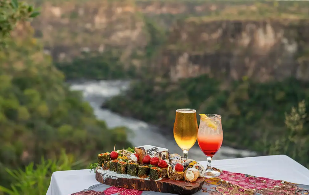 Tray with drinks and canapes on the gorge edge, warm late-afternoon light, gorge walls visible below. Atmospheric. People optional.