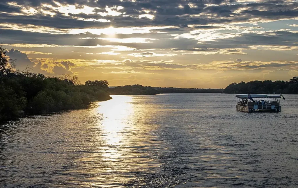 A Zambezi sunset cruise boat on calm water at golden hour above Victoria Falls