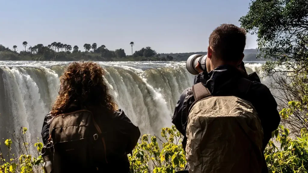 Visitors on a guided tour of Victoria Falls with rising spray and a rainbow over the gorge